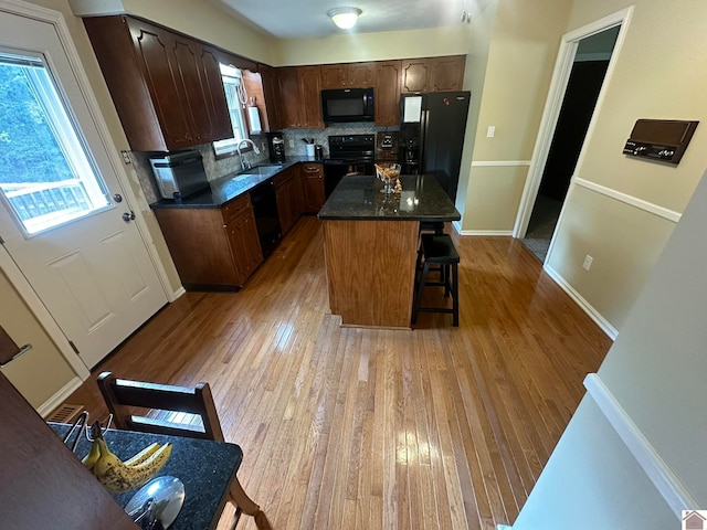 kitchen featuring a kitchen bar, light wood-type flooring, black appliances, sink, and a center island