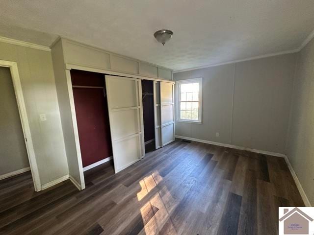 unfurnished bedroom featuring a closet, dark wood-type flooring, and ornamental molding