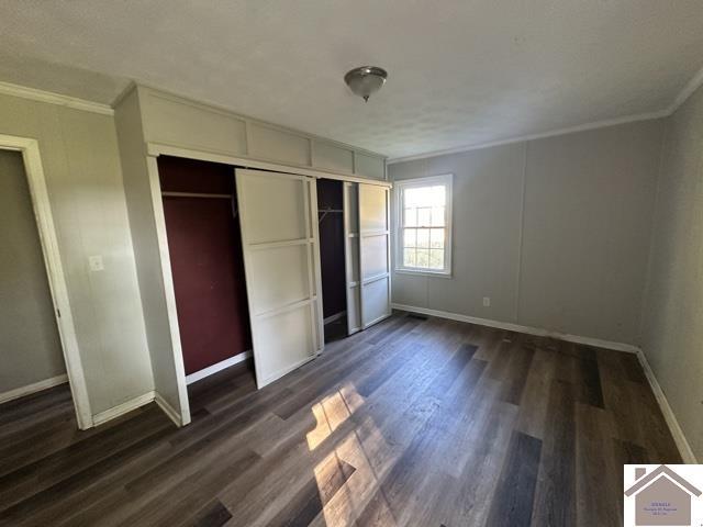 unfurnished bedroom with a closet, crown molding, baseboards, and dark wood-style flooring