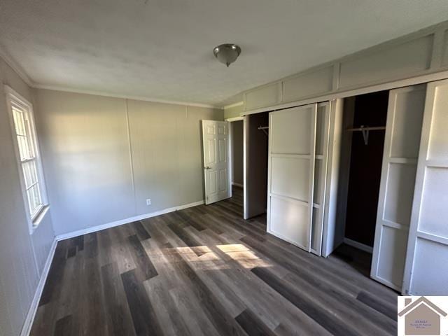 unfurnished bedroom with baseboards, ornamental molding, dark wood-type flooring, and a closet