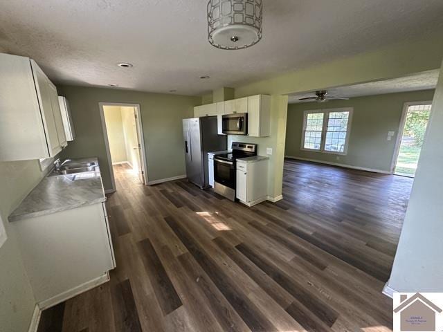 kitchen with white cabinets, stainless steel appliances, a ceiling fan, dark wood-type flooring, and baseboards