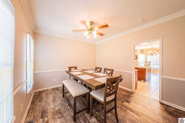 dining space featuring dark wood-type flooring, crown molding, and ceiling fan with notable chandelier