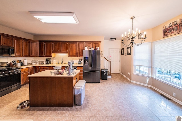 kitchen featuring tasteful backsplash, appliances with stainless steel finishes, an inviting chandelier, a center island, and decorative light fixtures