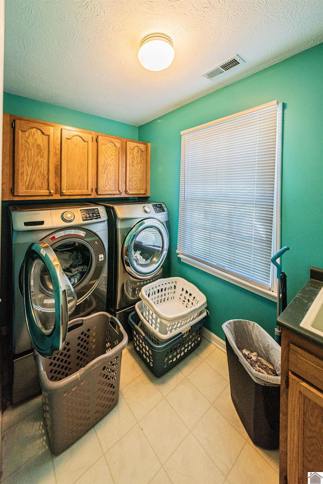 clothes washing area with washer and dryer, a textured ceiling, and cabinets