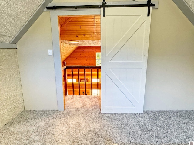 additional living space with vaulted ceiling, carpet flooring, a barn door, and wood walls