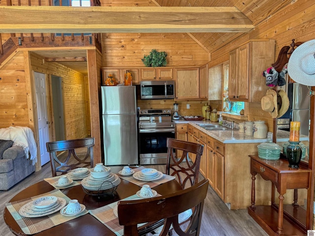 kitchen with sink, lofted ceiling with beams, stainless steel appliances, wooden walls, and hardwood / wood-style flooring