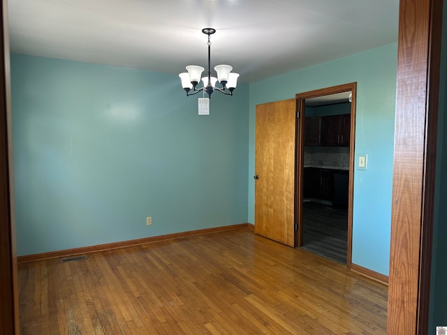 unfurnished room with a chandelier and hardwood / wood-style flooring