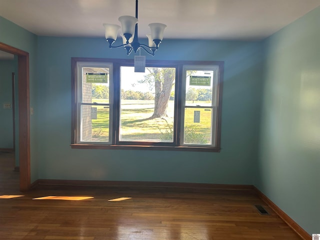 unfurnished dining area featuring a notable chandelier, a healthy amount of sunlight, and dark hardwood / wood-style flooring