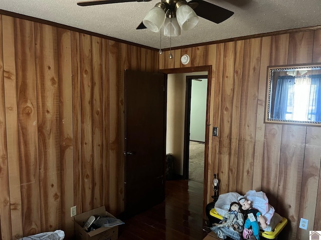 bedroom featuring ceiling fan, a textured ceiling, dark hardwood / wood-style flooring, and wooden walls