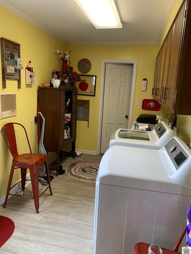 clothes washing area featuring crown molding, washing machine and dryer, light hardwood / wood-style flooring, and cabinets