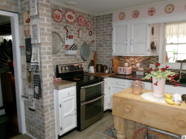 kitchen featuring range with two ovens, backsplash, white cabinetry, light hardwood / wood-style floors, and ornamental molding