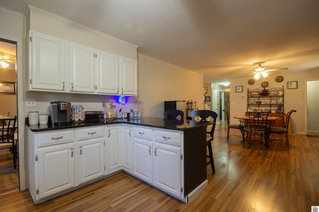 kitchen featuring kitchen peninsula, white cabinets, ceiling fan, dark stone countertops, and dark wood-type flooring