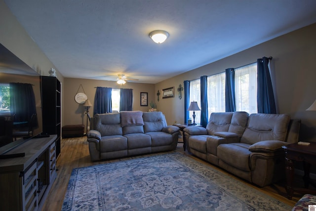 living room featuring dark wood-type flooring, ceiling fan, and plenty of natural light