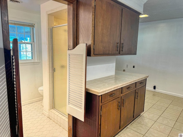 kitchen featuring tile counters, dark brown cabinetry, and light tile patterned flooring