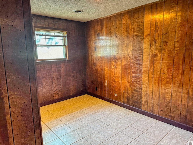 tiled empty room featuring a textured ceiling and wooden walls