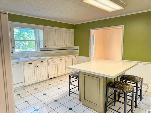 kitchen with a kitchen island, a kitchen breakfast bar, white dishwasher, ornamental molding, and sink