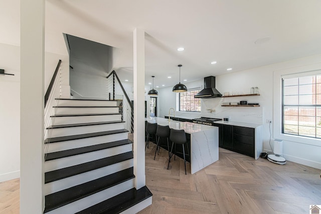 kitchen featuring wall chimney exhaust hood, a spacious island, light parquet flooring, and plenty of natural light