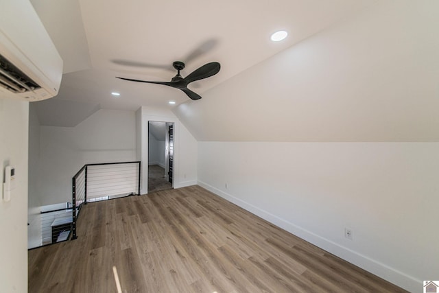 additional living space with hardwood / wood-style flooring, an AC wall unit, ceiling fan, and vaulted ceiling