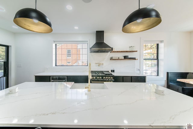 kitchen featuring light stone counters, high end black range oven, sink, wall chimney exhaust hood, and decorative light fixtures