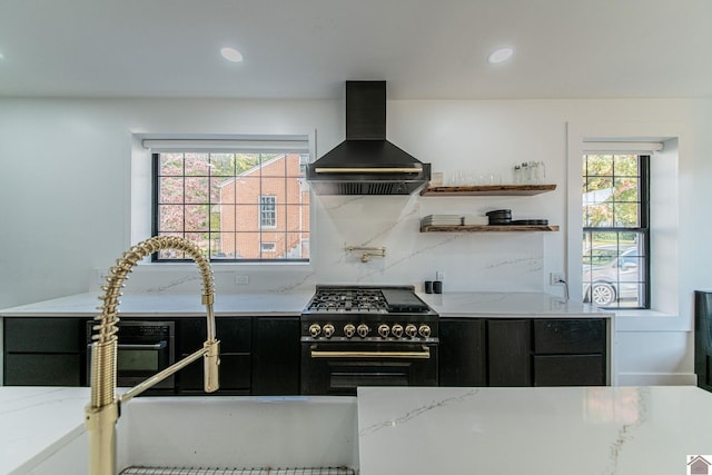 kitchen with wall chimney exhaust hood, a healthy amount of sunlight, stainless steel stove, and light stone counters