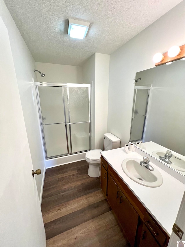 bathroom with toilet, hardwood / wood-style floors, a shower with shower door, and vanity