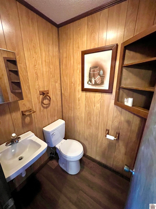 bathroom featuring sink, a textured ceiling, toilet, wooden walls, and hardwood / wood-style flooring