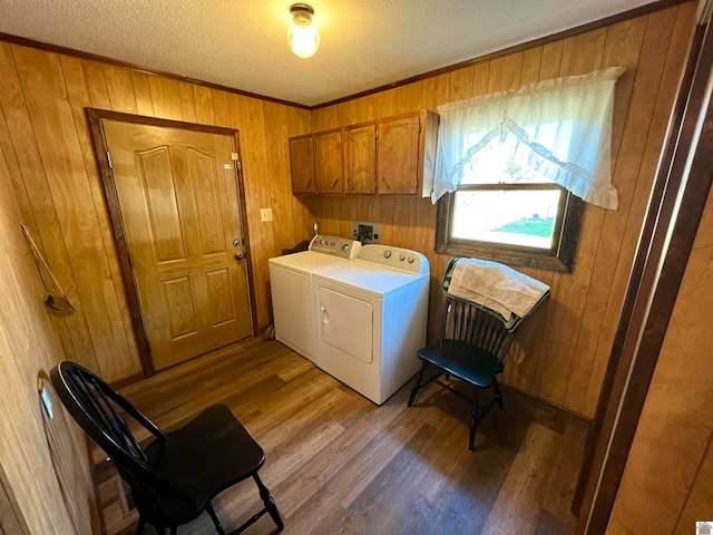 laundry room featuring wood walls, wood-type flooring, a textured ceiling, washer and clothes dryer, and cabinets