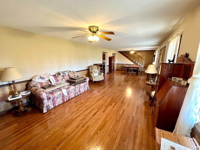 living room featuring hardwood / wood-style floors, ceiling fan, wooden walls, and a textured ceiling