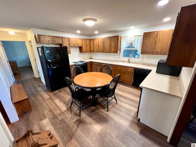 kitchen featuring a textured ceiling, wood-type flooring, black appliances, crown molding, and sink