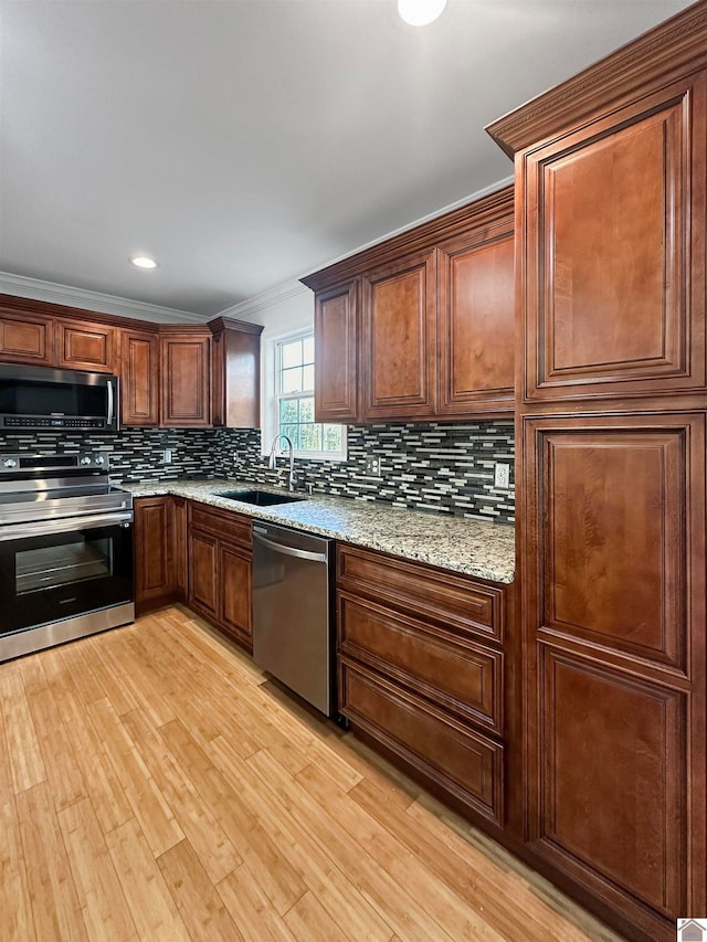 kitchen with backsplash, sink, appliances with stainless steel finishes, light stone counters, and light hardwood / wood-style floors