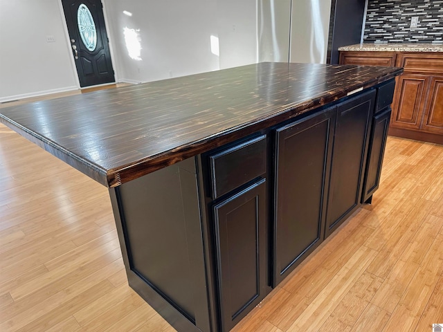 kitchen with light wood-type flooring, a kitchen island, stainless steel fridge, dark stone countertops, and decorative backsplash