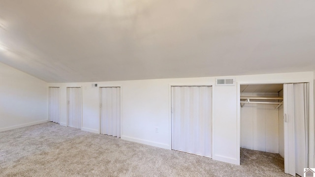 unfurnished bedroom featuring light colored carpet, vaulted ceiling, and two closets