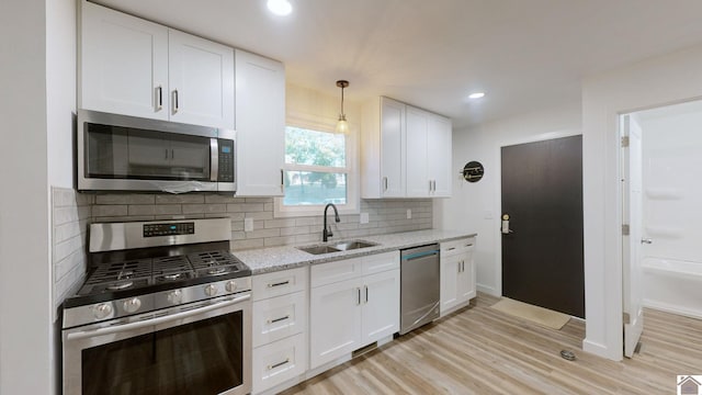 kitchen with stainless steel appliances, sink, light stone countertops, light wood-type flooring, and white cabinets