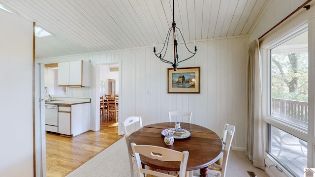 dining room with wood ceiling, wooden walls, and light hardwood / wood-style floors