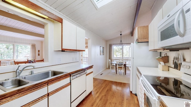 kitchen with white cabinets, hanging light fixtures, lofted ceiling with skylight, sink, and white appliances