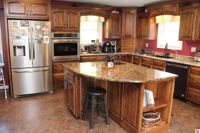 kitchen featuring appliances with stainless steel finishes, a healthy amount of sunlight, sink, and a center island with sink