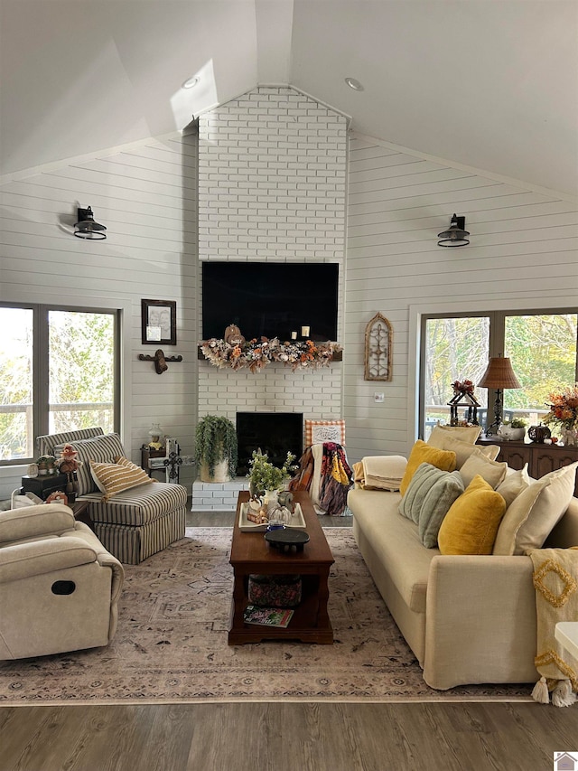 living room with wood walls, hardwood / wood-style flooring, high vaulted ceiling, and a brick fireplace