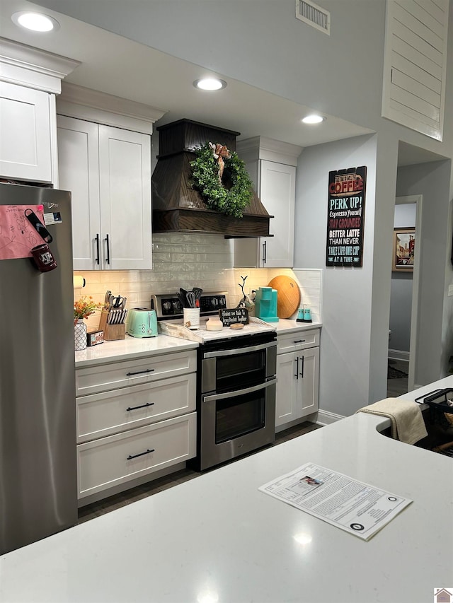 kitchen with appliances with stainless steel finishes, custom exhaust hood, white cabinetry, and backsplash