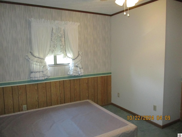 carpeted empty room featuring ornamental molding, wood walls, and ceiling fan