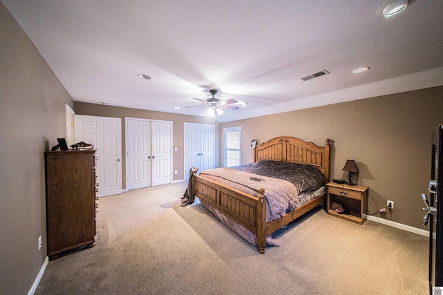 bedroom featuring ceiling fan, multiple closets, and light colored carpet