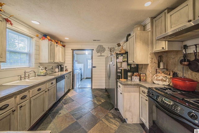 kitchen with wall chimney range hood, sink, light brown cabinetry, appliances with stainless steel finishes, and a textured ceiling