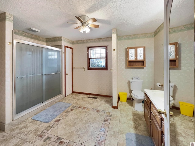 bathroom featuring a textured ceiling, a shower with shower door, toilet, ceiling fan, and vanity