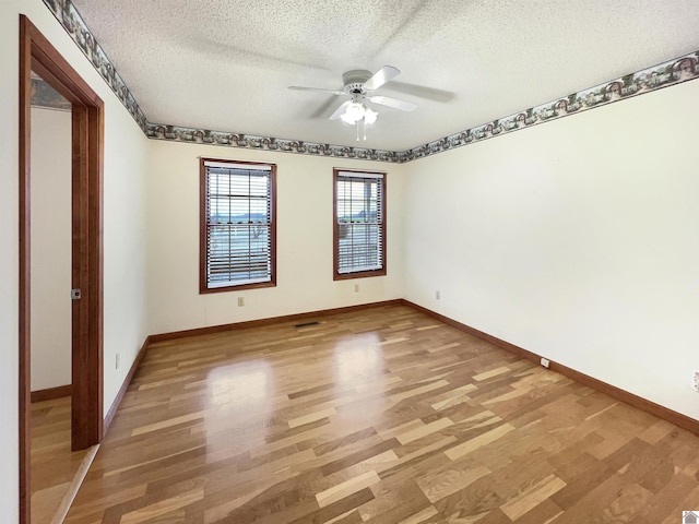empty room with baseboards, a ceiling fan, light wood finished floors, and a textured ceiling
