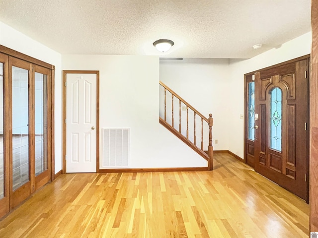 entryway with baseboards, a textured ceiling, light wood-style flooring, and visible vents