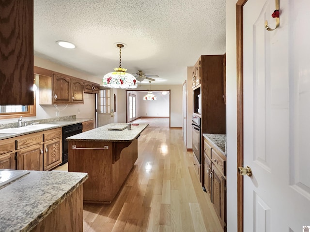kitchen with a sink, a textured ceiling, a kitchen island, and black appliances