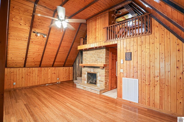 unfurnished living room with vaulted ceiling with beams, wooden ceiling, light wood-type flooring, a fireplace, and wood walls