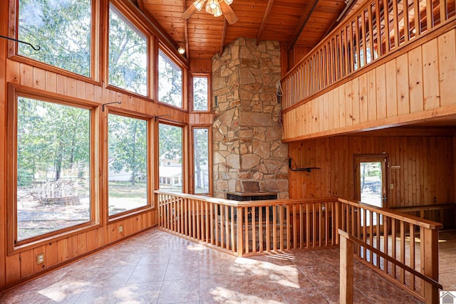 unfurnished sunroom featuring a stone fireplace, lofted ceiling with beams, wooden ceiling, and ceiling fan