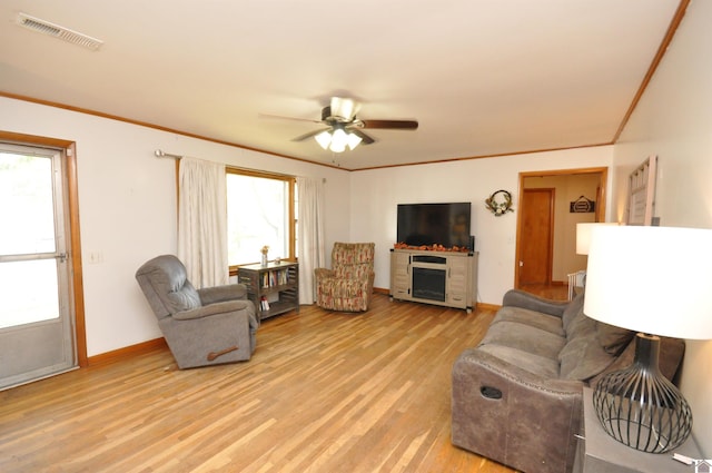 living room featuring ceiling fan, ornamental molding, light wood-type flooring, and a fireplace