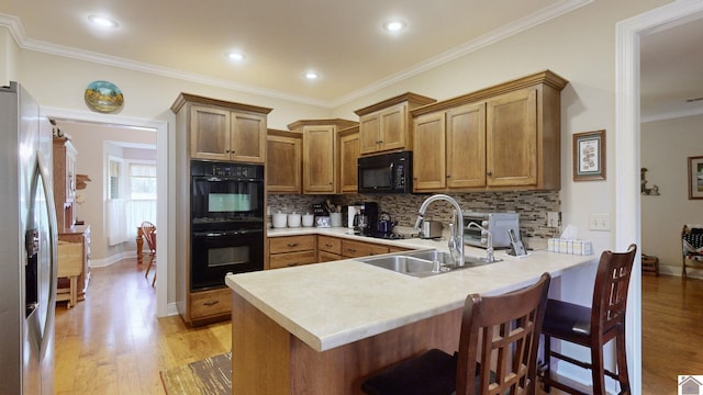 kitchen featuring light hardwood / wood-style flooring, kitchen peninsula, black appliances, and sink