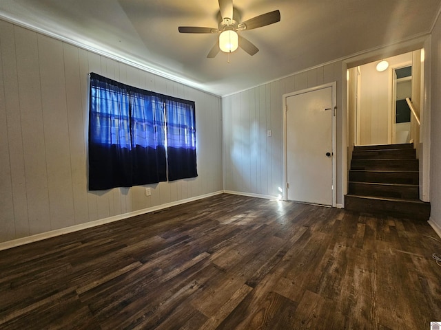 empty room featuring ceiling fan, wooden walls, and dark hardwood / wood-style floors